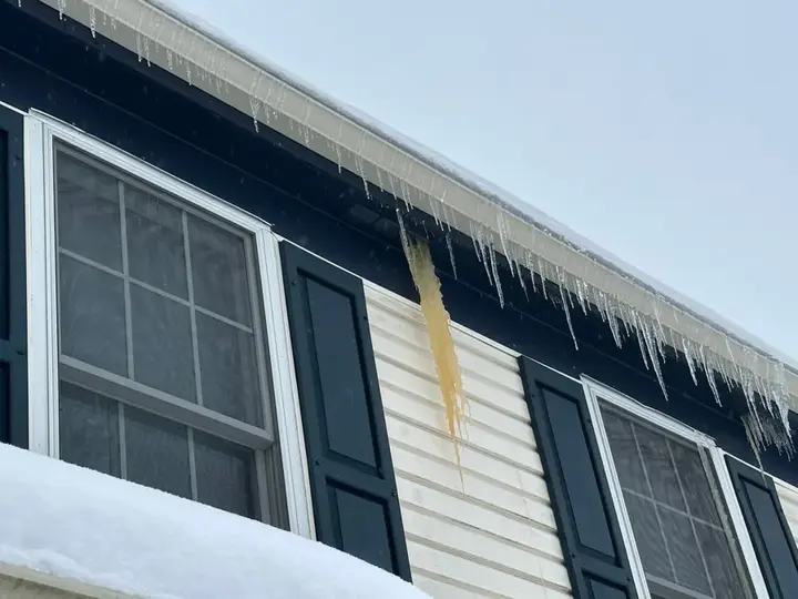 Ice dam meltwater staining the siding below a snow-covered roof edge
